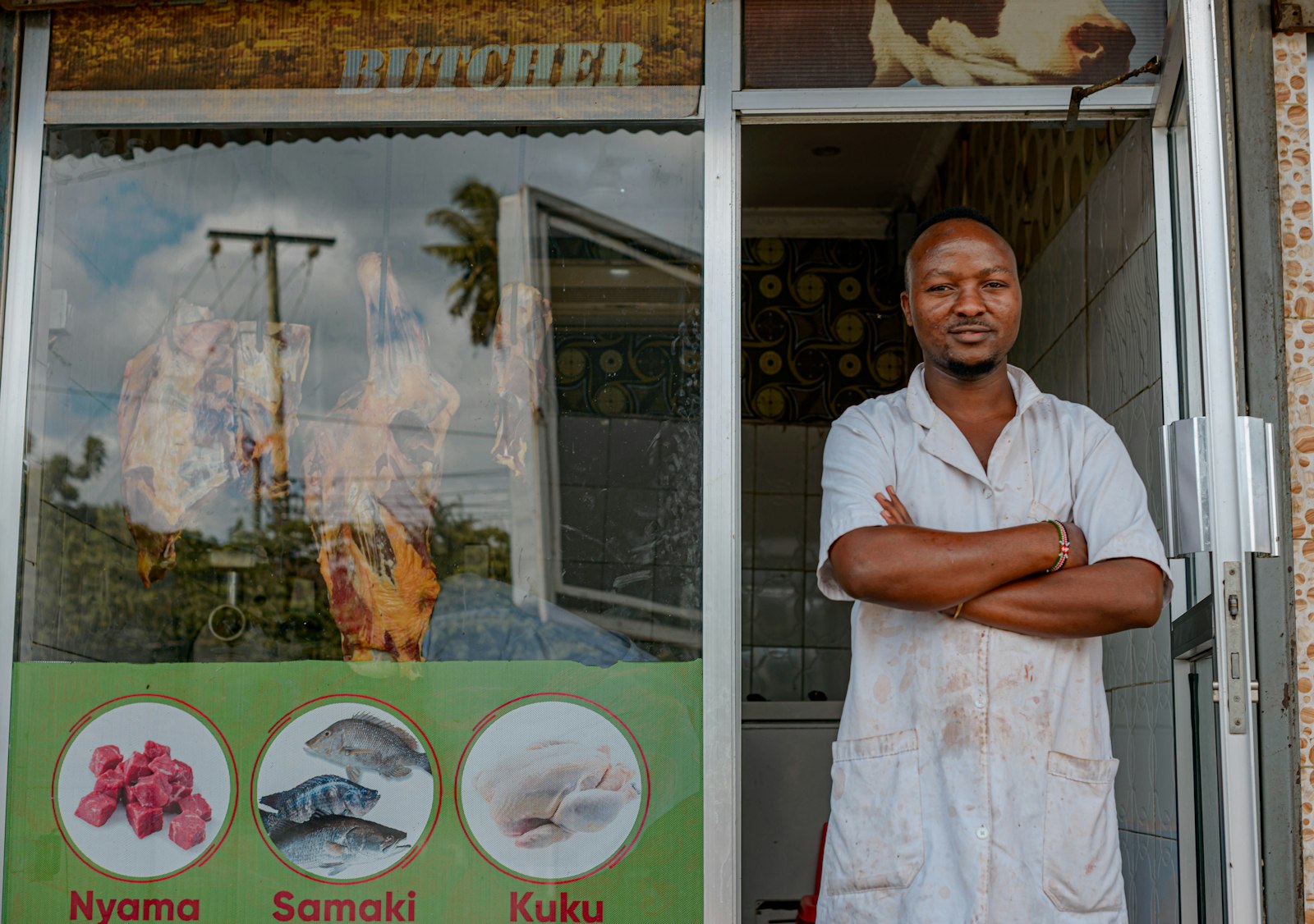 Shop owner standing with arms crossed outside a butchery