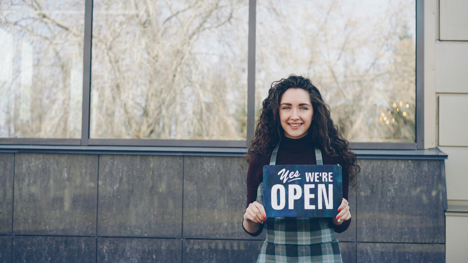 Small business owner smiling and holding a Yes, we're open sign